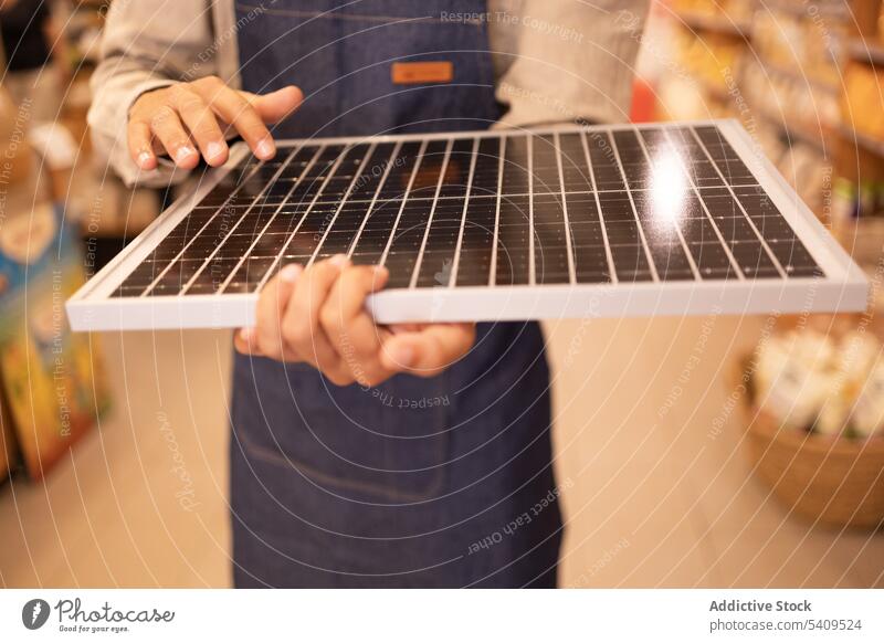 Anonymous crop seller holding portable solar panel in store man supermarket shop worker purchase modern device shopper energy generation male gadget alternative