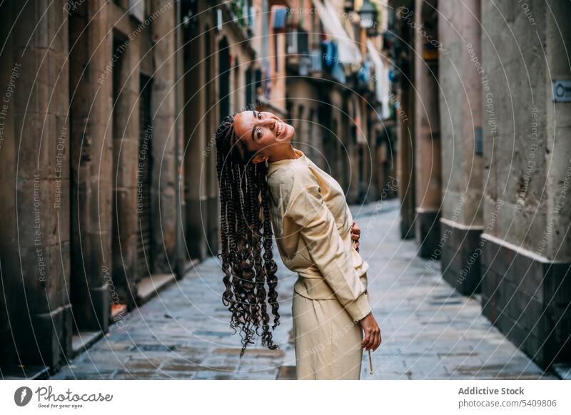 Stylish smiling woman standing on city street smile style braid outfit town cheerful happy hairstyle narrow female joy positive building charming glad attire