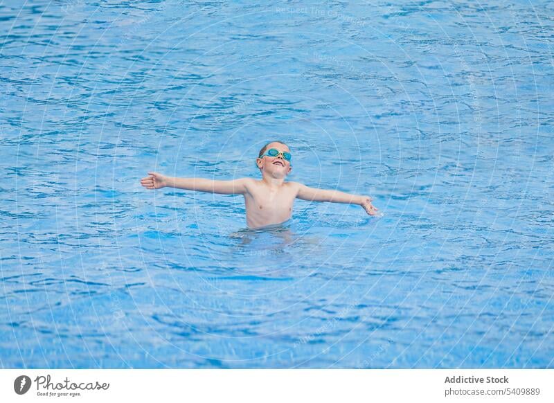 Cheerful cute kid in goggles standing in swimming pool and playing alone child happy glad smile enjoy water summer boy wet hair pastime cheerful positive