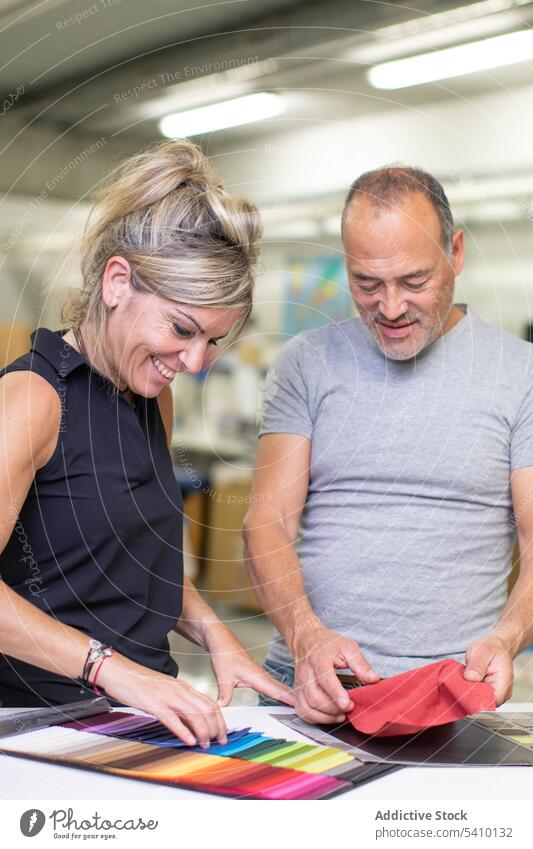 Happy middle aged man and adult woman examining colorful fabric samples in daylight smile manufacture factory examine quality textile check male mature female