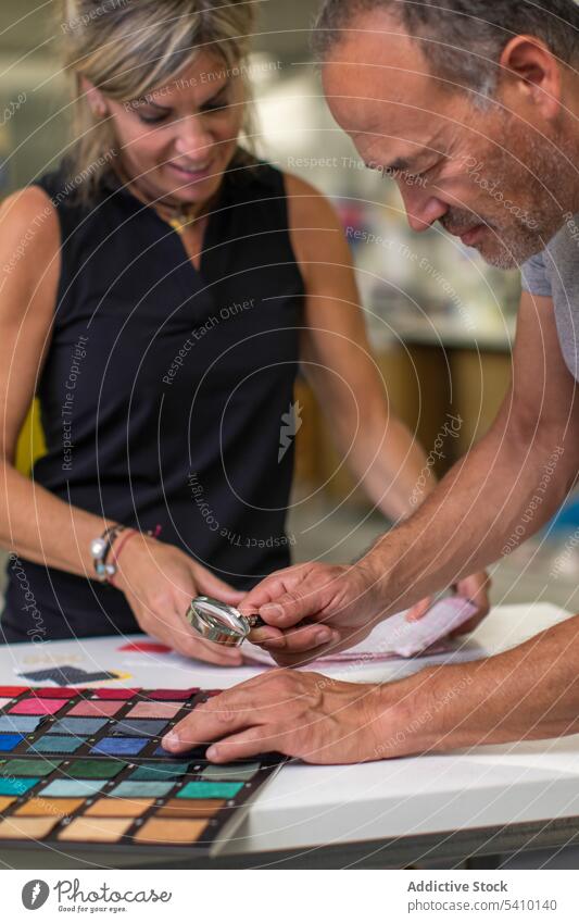 Serious man using magnifier at desk to check fabric texture and quality examine tool magnifying glass professional explore analyze workplace worker employee