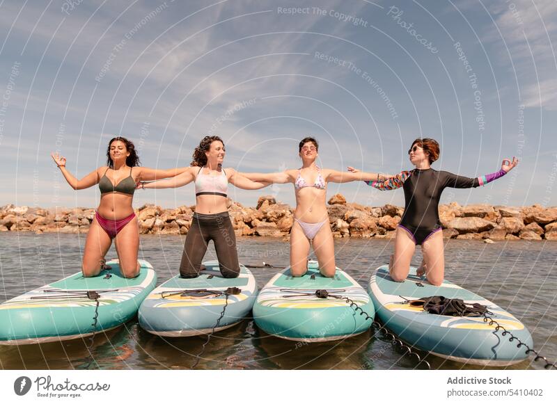 Group of young women in bikinis kneeling on paddleboards in daylight group smile together holding hands swimwear yoga positive female friend summer happy cloudy