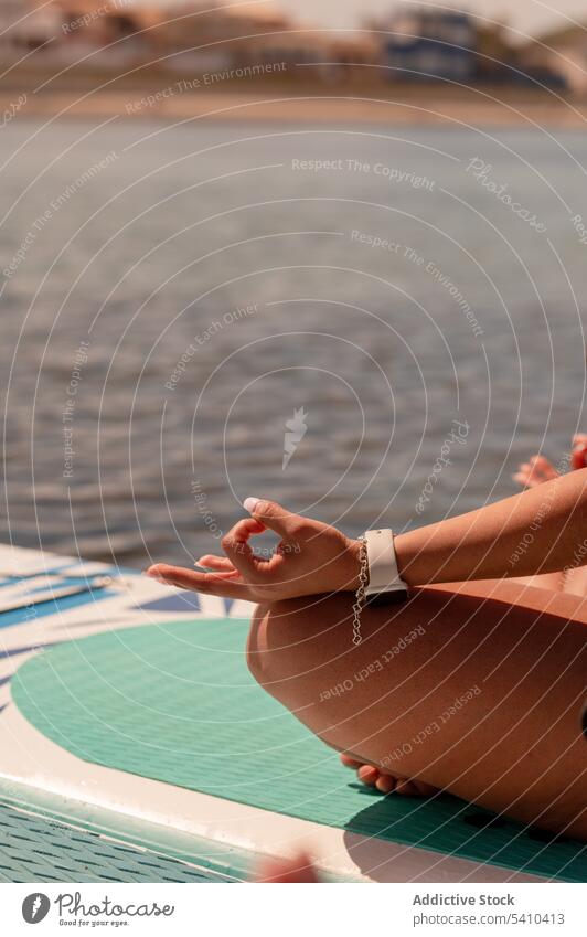 Crop lady meditating on SUP board in serene sea sup yoga paddleboard gyan mudra sup board woman meditate balance seaside zen practice calm harmony pose wellness