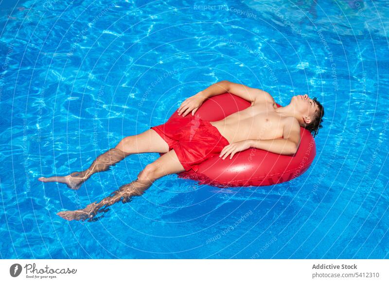 Positive teen boy lying in floater over swimming pool kid water resort smile content child enjoy childhood carefree chill recreation vacation positive preteen