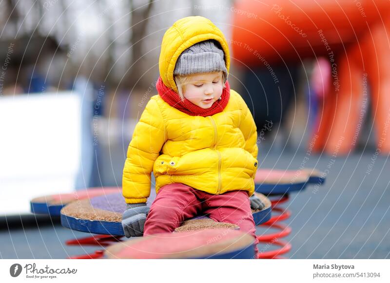 Cute little boy having fun on outdoor playground winter cold kid toddler day wooden equipment teeter seesaw wobble playtime casual outdoors portrait autumn