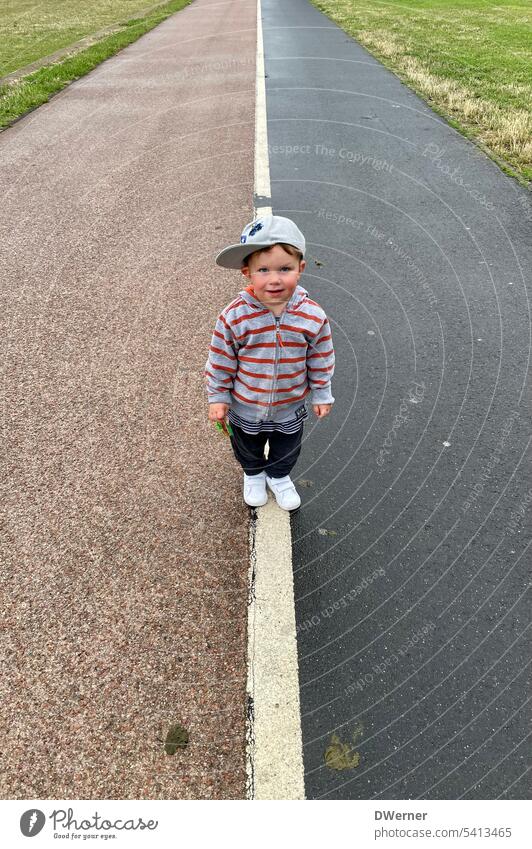 Child on sidewalk off Line Asphalt Cap 2 years Red White Black Street Exterior shot Signs and labeling Colour photo Transport Gray Stripe decide Decide Jacket