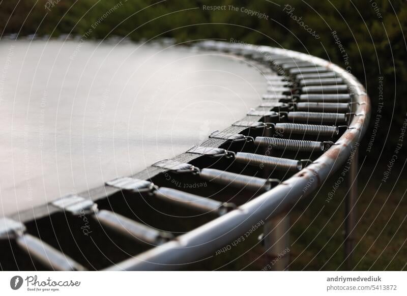 Recreation area. Modern opened trampoline without barrier, metal construction with springs, close up outdoors at backyard. Active summer holiday, fitness training in the fresh air. Happy childhood