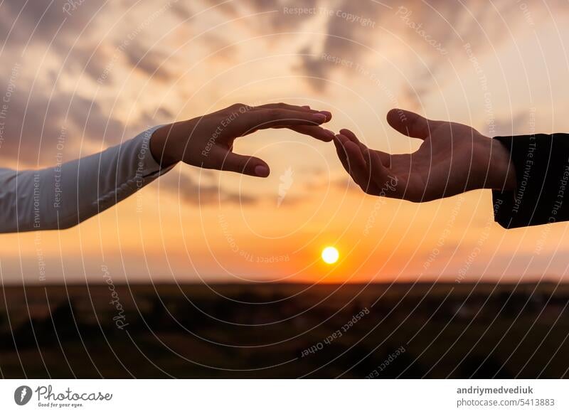 Hands of bride and groom reaching each other, touching fingers on sunset sky countryside background. Helping hands for save and support people concept. Wedding day. Valentine day.