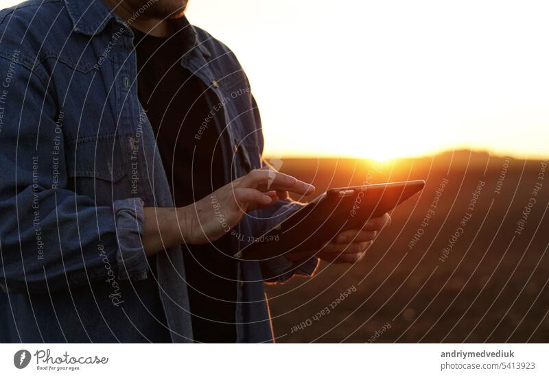 Cropped shot of male farmer's hands use digital tablet on plowed field for control of soil quality, land readiness for sowing crops and planting vegetables. Smart farming technology and agriculture