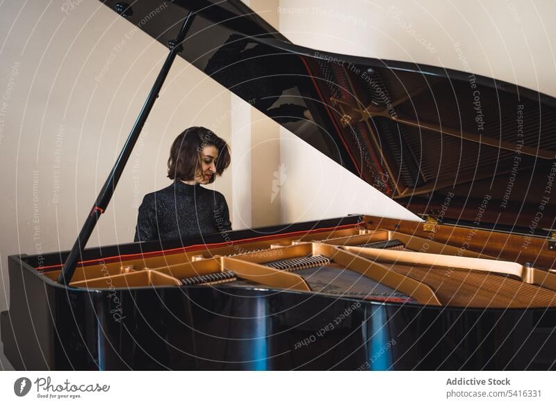 Young woman playing notes behind a piano musician young slim elegant room pianist instrument keyboard art sound performance female melody classical closed eyes