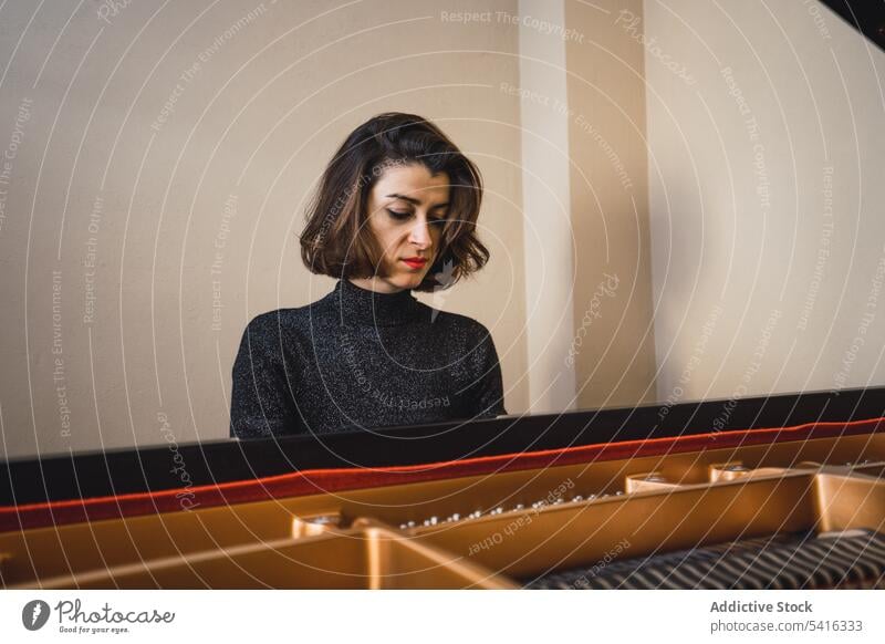 Young woman playing notes behind a piano musician young slim elegant room pianist instrument keyboard art sound performance female melody classical closed eyes