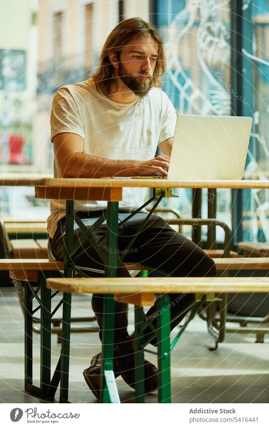 Handsome man sitting at table and typing on laptop handsome mustache working adult lifestyle stubble hairstyle happiness bearded model young confident