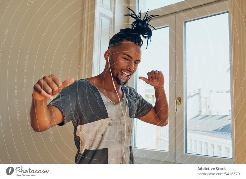 Cheerful ethnic male listening to music man hairstyle cornrows braided earphones dance thumbs up young african american person handsome positive attractive