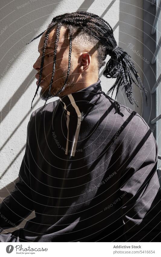 Stylish ethnic male sitting on railing man braid hairstyle pigtails cornrows trendy staircase young african american person handsome attractive thoughtful