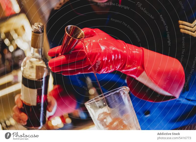 Bartender in red gloves pouring drink to bottle bartender mixing alcohol nightclub stirring preparing barman cocktail uniform ice cubes glass beverage alcoholic