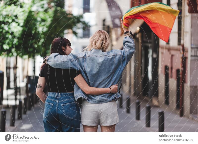 Lesbian couple with LGBT flag walking on street lesbian lgbt hugging happy waving city young together women casual homosexual pride equality alternative