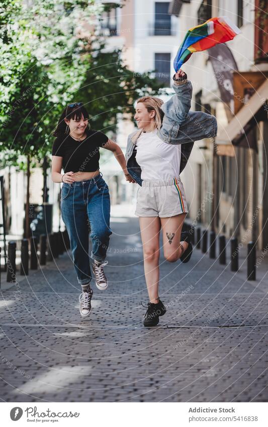 Lesbian couple with LGBT flag walking on street lesbian lgbt happy waving city young together women casual homosexual pride equality alternative relationship