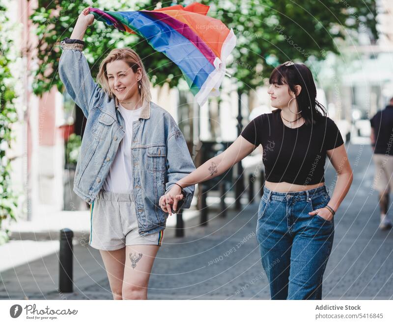 Lesbian couple with LGBT flag walking on street lesbian lgbt happy waving city young together women casual homosexual pride equality alternative relationship