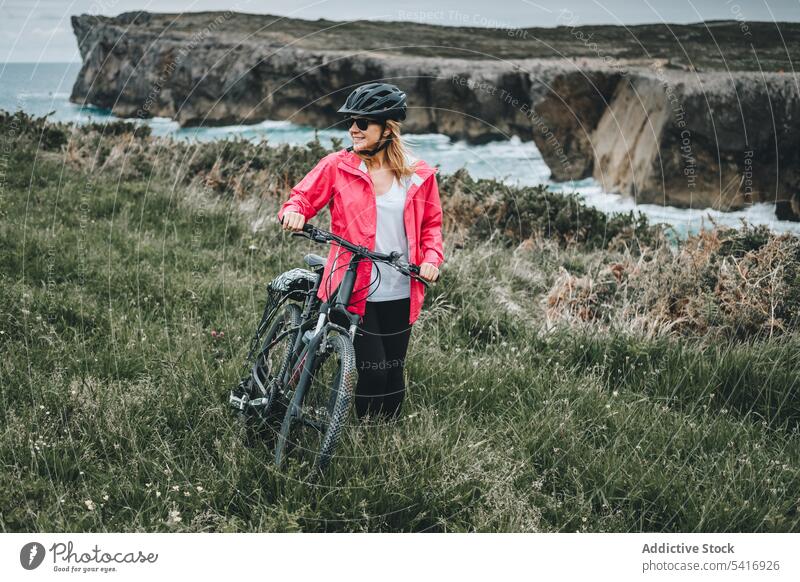 Female bicyclist on rocks woman bicycle cliff helmet sea landscape extreme female young person cheerful active sportive smiling walking lifestyle ride bike