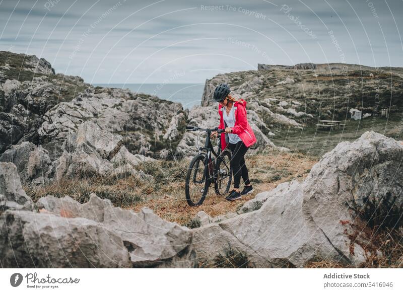 Female bicyclist on rocks woman bicycle cliff helmet sea landscape extreme female young person cheerful active sportive smiling walking lifestyle ride bike