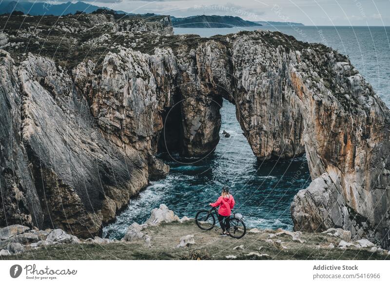 Female bicyclist on rocks woman bicycle cliff anonymous helmet sea landscape extreme female young person sportive smiling walking lifestyle ride bike travel