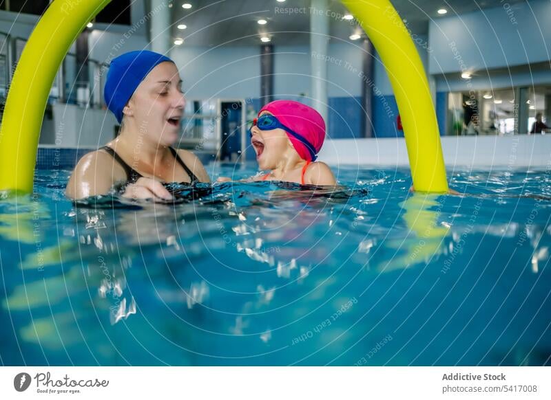 Cheerful girl swimming in pool with mother water park excited fun weekend together amusement woman kid child goggles hat cheerful happy resort family daughter