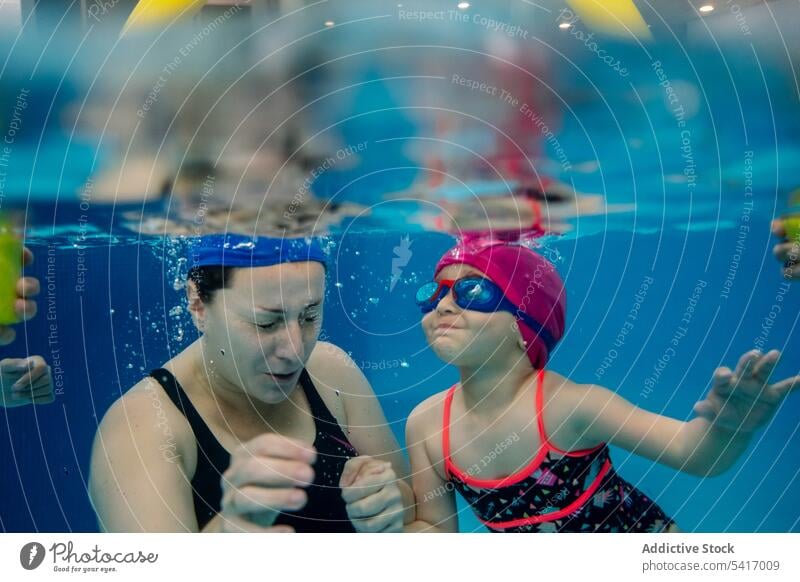 Cheerful girl underwater swimming in pool with mother park excited fun weekend together amusement woman kid child goggles hat cheerful happy resort family