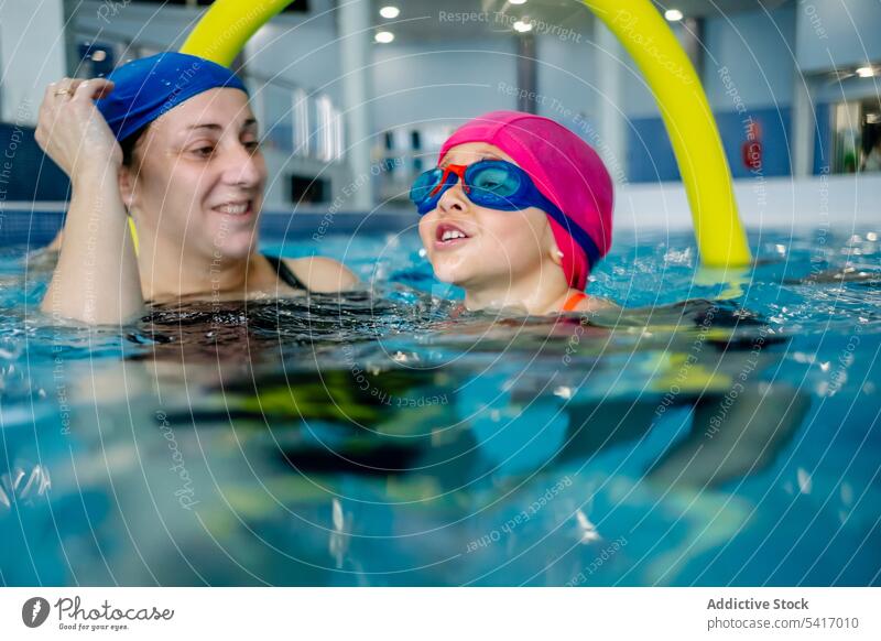 Cheerful girl swimming in pool with mother water park excited fun weekend together amusement woman kid child goggles hat cheerful happy resort family daughter