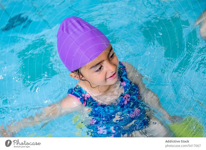 Wet girl standing on poolside wet looking away swimming hat goggles swimwear ethnic little kid child water park drops swimsuit leisure rest relax resort joy fun