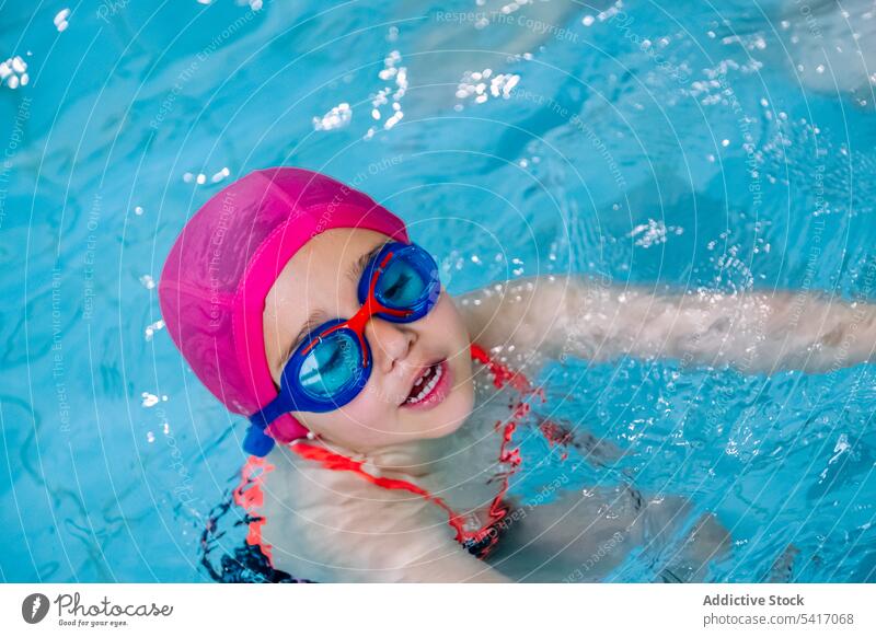 Wet girl standing on poolside wet looking away swimming hat goggles swimwear ethnic little kid child water park drops swimsuit leisure rest relax resort joy fun