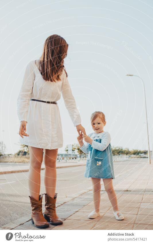 Mother and daughter standing on street mother city sidewalk holding hands family together sky cloudless blue woman girl kid child mom parent pavement town