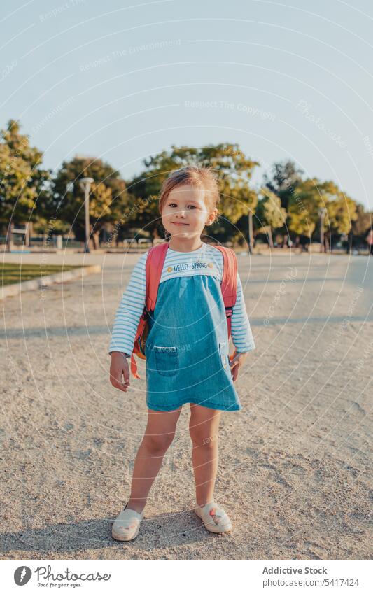 Little girl standing in park smiling little sand lifestyle leisure backpack casual happy kid child sunny daytime weekend rest relax summer preschooler stylish