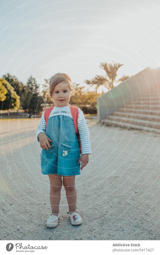 Little girl standing in park smiling little sand lifestyle leisure backpack casual happy kid child sunny daytime weekend rest relax summer preschooler stylish