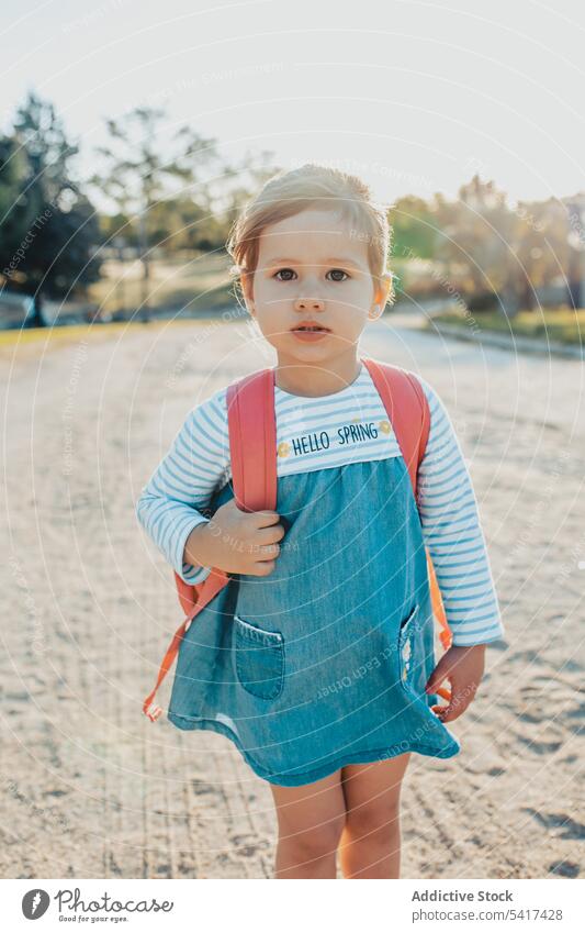 Little girl standing in park smiling little sand lifestyle leisure backpack casual happy kid child sunny daytime weekend rest relax summer preschooler stylish