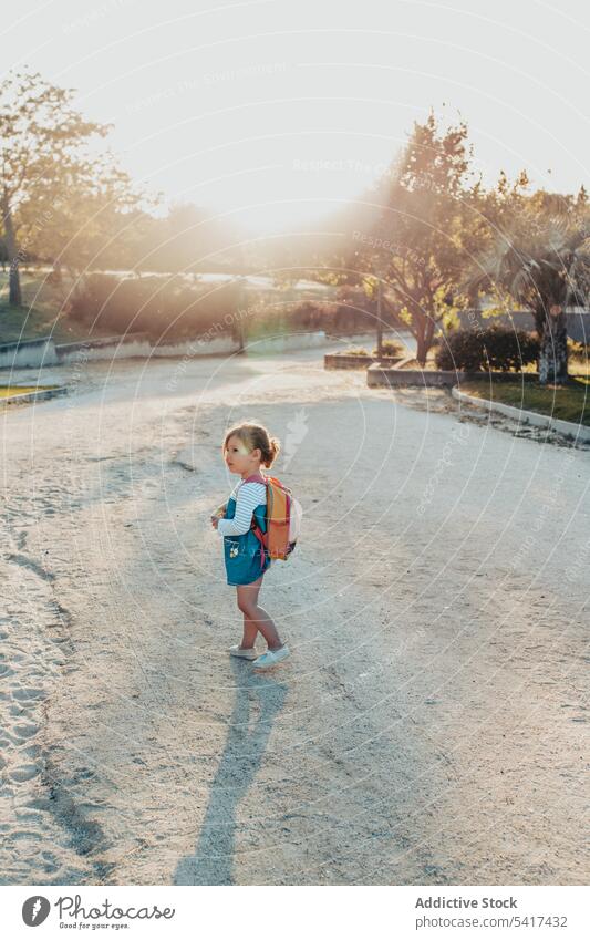 Little girl standing in park smiling little sand lifestyle leisure backpack casual happy kid child sunny daytime weekend rest relax summer preschooler stylish