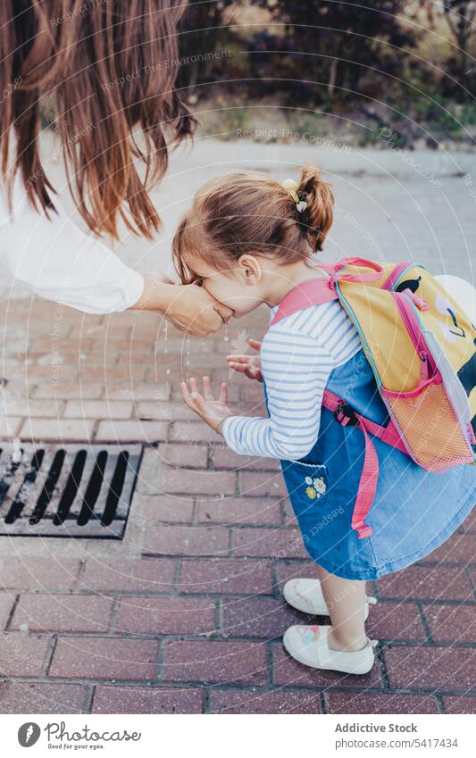 Crop mother giving water to daughter park drinking fountain handful clean washing pavement woman girl kid child family parent lifestyle leisure care thirsty joy