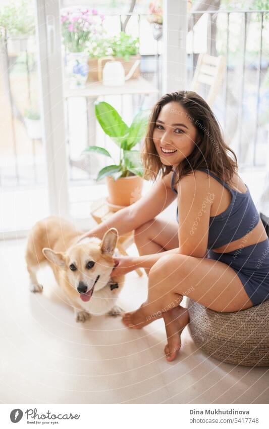 millennial caucasian woman at home with corgi dog. Dog owner and trainer. Funny cozy picture of female with puppy in apartment. Brunette smiling with welsh corgi Pembroke dog sitting on couch.