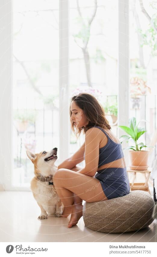 millennial caucasian woman at home with corgi dog. Dog owner and trainer. Funny cozy picture of female with puppy in apartment. Brunette smiling with welsh corgi Pembroke dog sitting on couch.