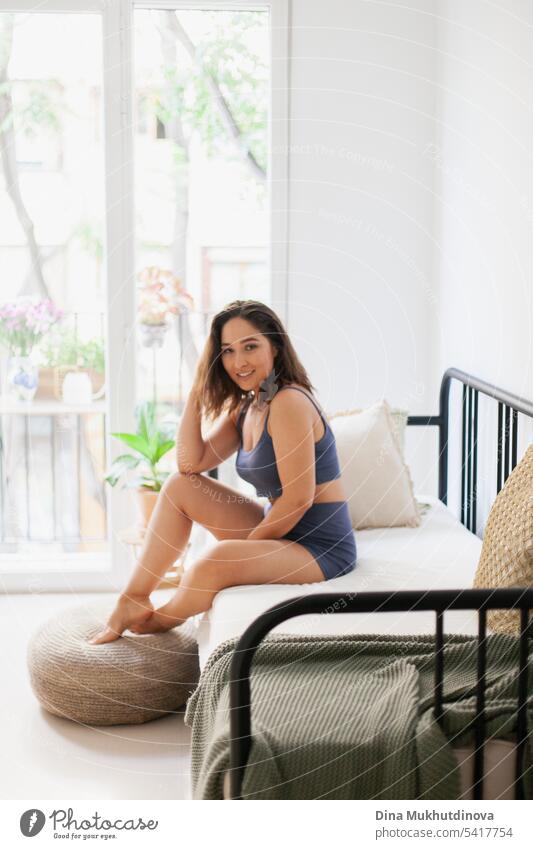 Happy young woman in minimal apartment lifestyle photo, smiling. Millennial woman at home. Interior shot with panoramic window. Girls pajama party. Good morning mood.