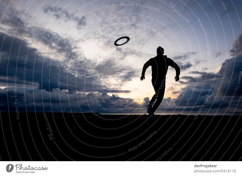 Man running towards frisbee in back light on beach Structures and shapes Nature reserve Subdued colour Copy Space left Copy Space right Copy Space top