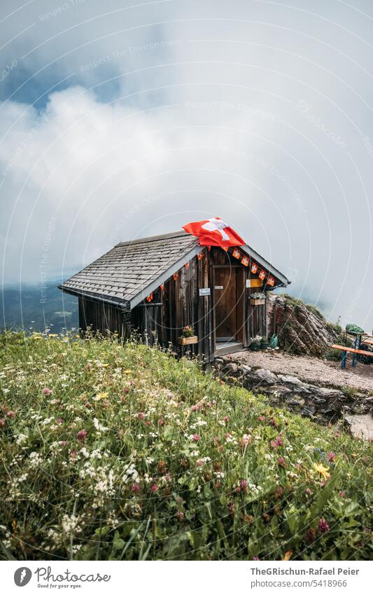 House with Swiss flag against cloudy background Grass big myths Chalet swiss flag Flag Switzerland Tourism Meadow Mountain Alps Colour photo Hiking Landscape