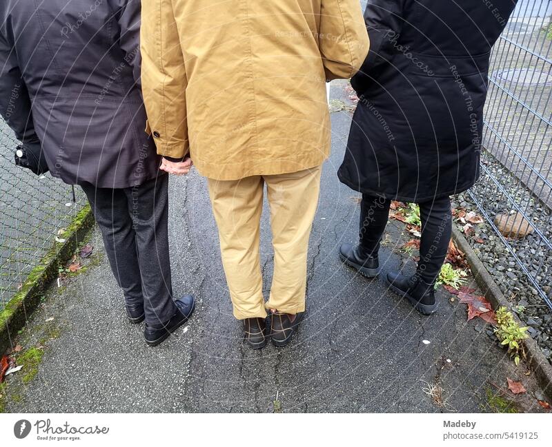 Women of different ages with jackets and coats in beige and black walking on wet asphalt in Oerlinghausen near Bielefeld at the Hermannsweg in the Teutoburg Forest in East Westphalia-Lippe