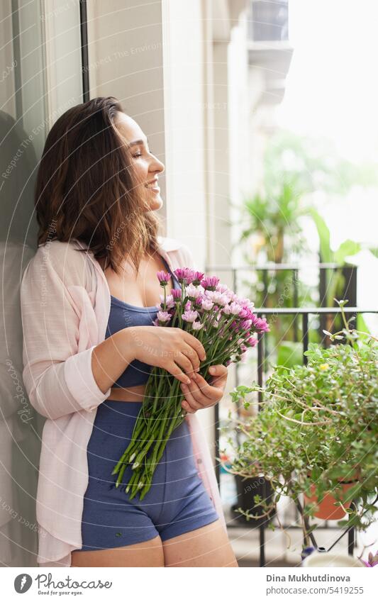 Beautiful woman with flowers bouquet on the balcony closeup. Happy brunette smiling. Plants and flowers gardening hobby. Balcony plant Balcony furnishings