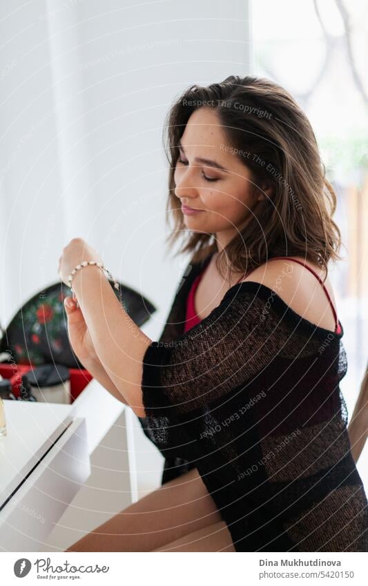 Woman putting on bracelet, getting dressed for party in red and black outfit using fan. Spanish vacation. Passionate sensual romantic female portrait in boudoir room. Summer heatwave.