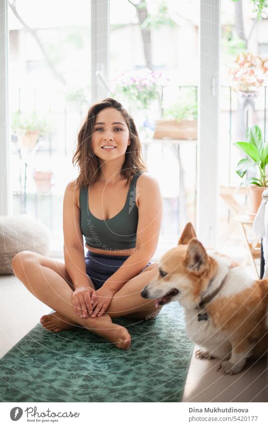 young woman with corgi Pembroke dog doing yoga on green mat at home. Practicing sport, wellness and healthcare. Indoor yoga online class. Mindfullnesss and meditation, active lifestyle.