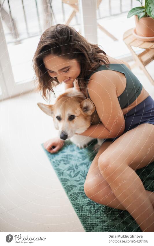 young woman with corgi Pembroke dog doing yoga on green mat at home. Practicing sport, wellness and healthcare. Indoor yoga online class. Mindfullnesss and meditation, active lifestyle.