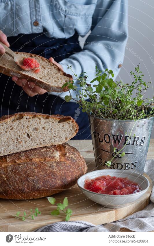 Anonymous woman preparing open sandwich with red sauce cooking spread bread sourdough kitchen spoon green plant meal food lunch breakfast morning lifestyle