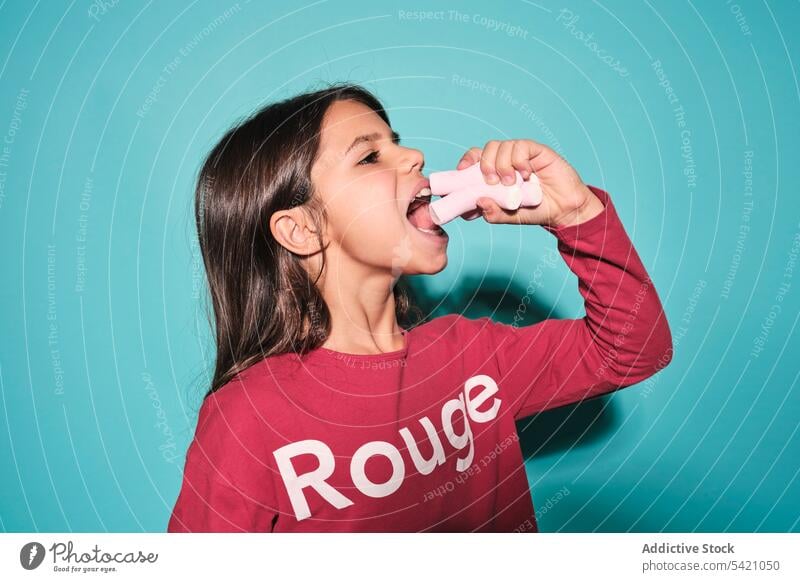 Little girl with marshmallow in studio kid eat candy enjoy sweet yummy child female tasty delicious modern brunette pleasure color trendy hungry craving little