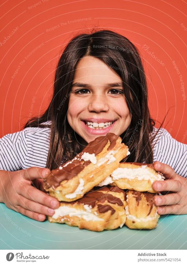 Happy girl with pile of eclairs kid candy eat happy craving sweet cheerful food enjoy child little yummy unhealthy calorie dessert pastry delicious tasty sugar