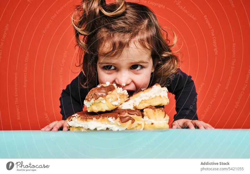 Happy girl with pile of eclairs kid candy eat happy craving sweet cheerful food enjoy child little yummy unhealthy calorie dessert pastry delicious tasty sugar